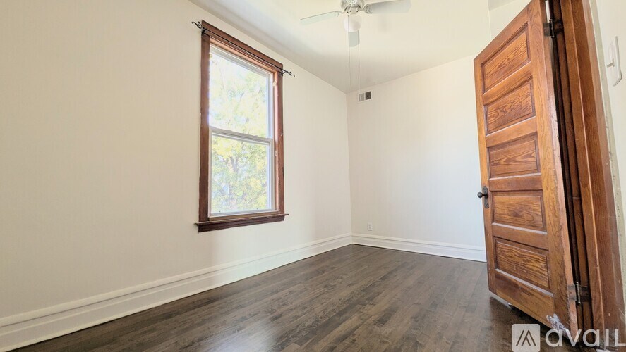 A room with a wooden floor, a window, and a door.