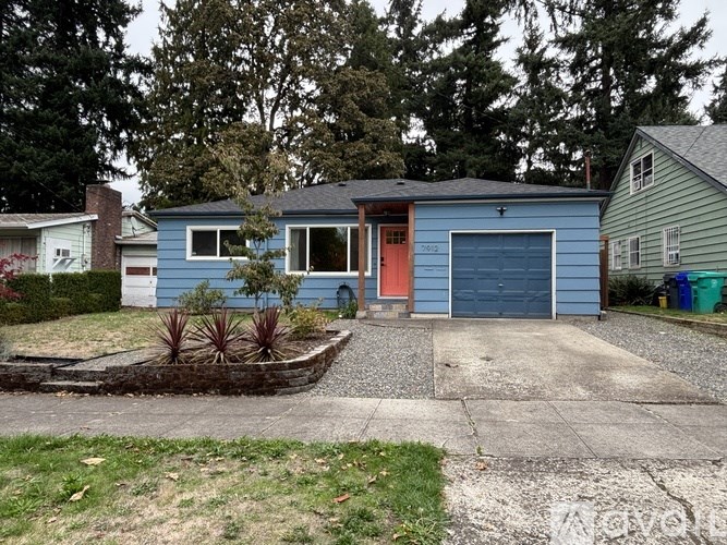 A blue house with a red door is surrounded by greenery.