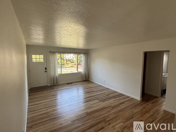 A room with wooden flooring and a window with white curtains.