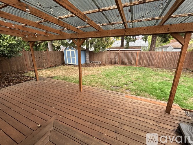 A wooden deck with a roof and a blue shed in the background.