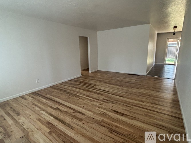 A room with wooden flooring and white walls, with a doorway leading to another room.