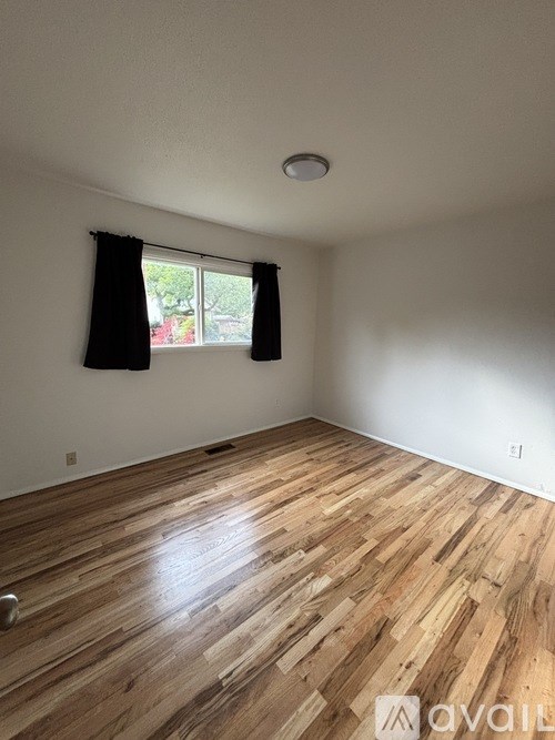 A room with wooden flooring and a window with black curtains.