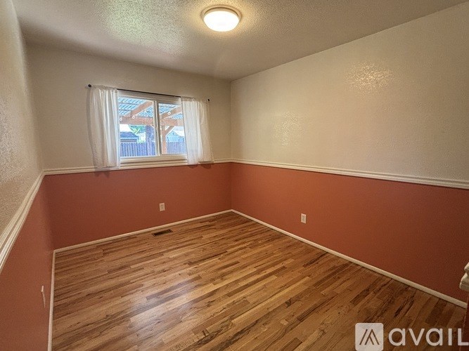 A room with wooden flooring and a window with white curtains.