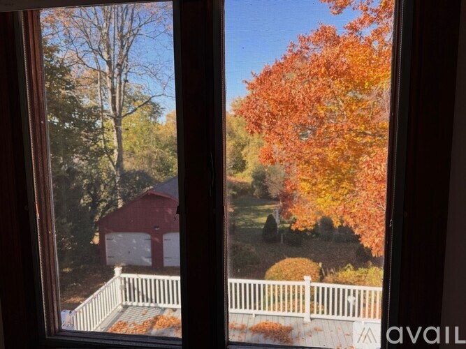 A view of a house through a window with a white fence and trees in the background.
