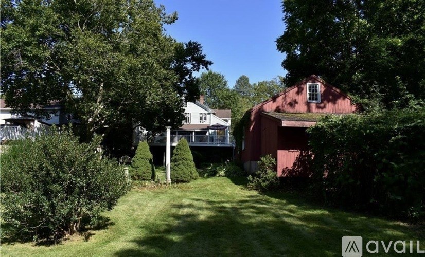 A red barn sits behind a white house with a green lawn in front.