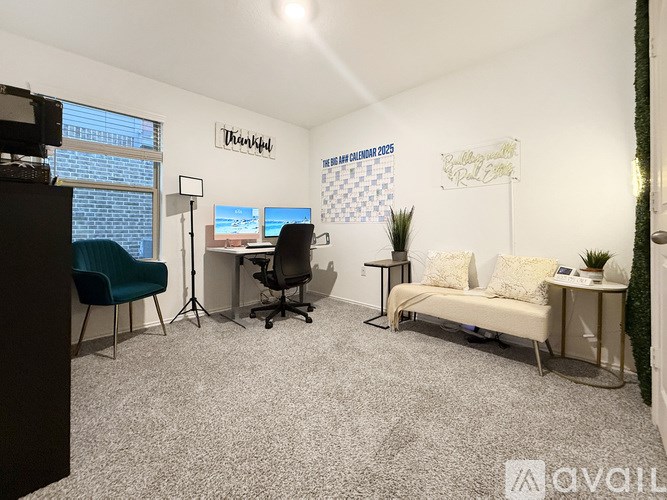 A room with a carpeted floor, a desk with a computer, a chair, a couch, and a plant.