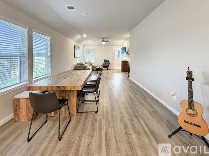 A room with a wooden floor, a long table with chairs, and a guitar on a stand.