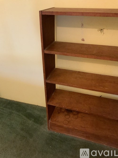 A brown shelf unit with four shelves is against a white wall.