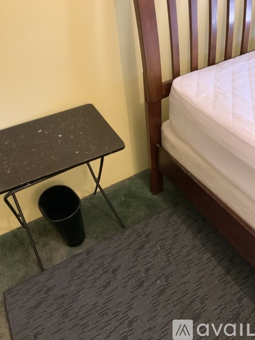 A small black table with a cup on it sits next to a bed.