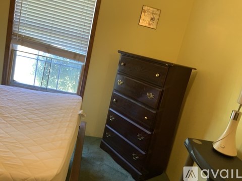 A bedroom with a bed, a dresser, and a window with blinds.