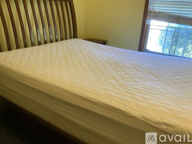 A bed with a white quilted cover is in the foreground with a striped headboard and a window in the background.