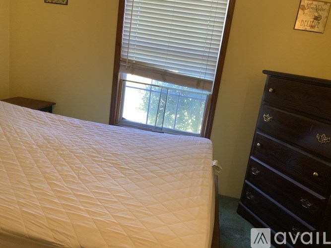 A bedroom with a white bedspread and a wooden dresser.