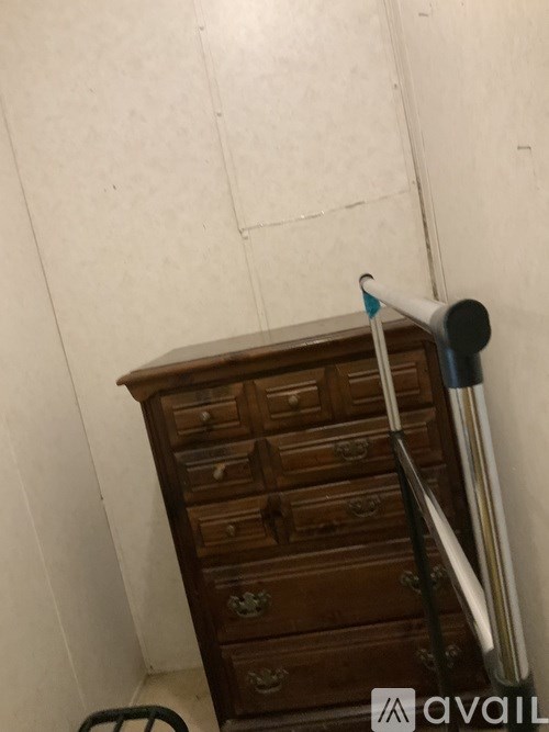 A tall wooden chest of drawers stands next to a white wall.
