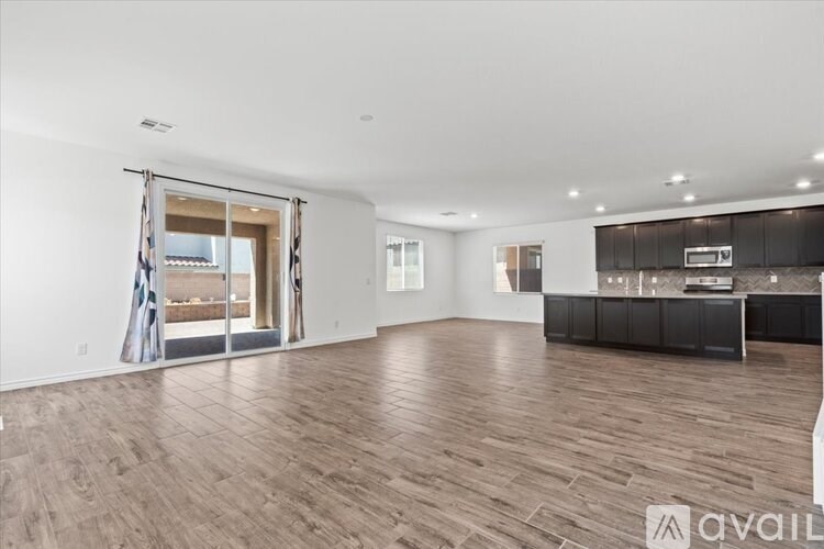 A spacious living room with hardwood floors and a kitchen area in the background.