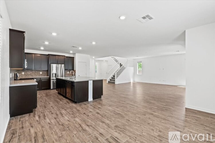 A spacious kitchen with dark wood floors and a staircase in the background.