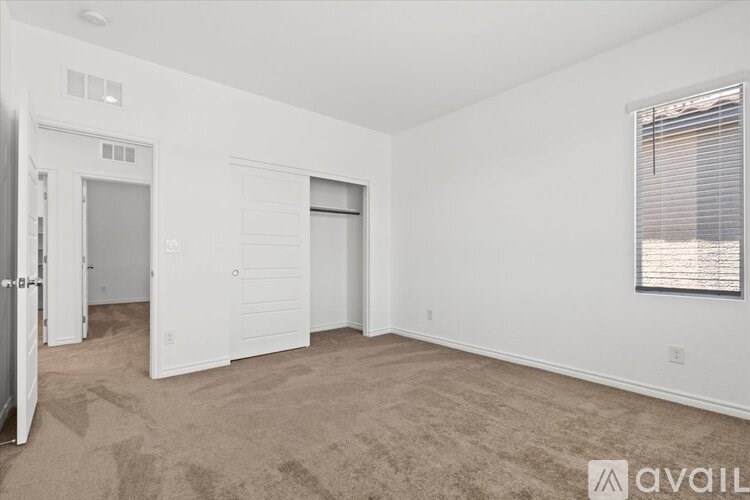 A sparsely furnished room with a carpeted floor and a window with blinds.