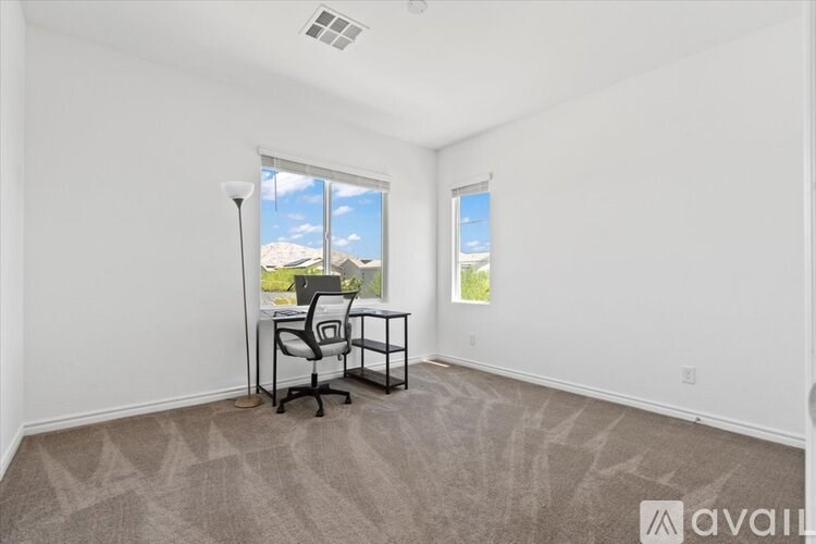 A room with a carpeted floor, a desk with a chair, and a window showing a view of the outdoors.