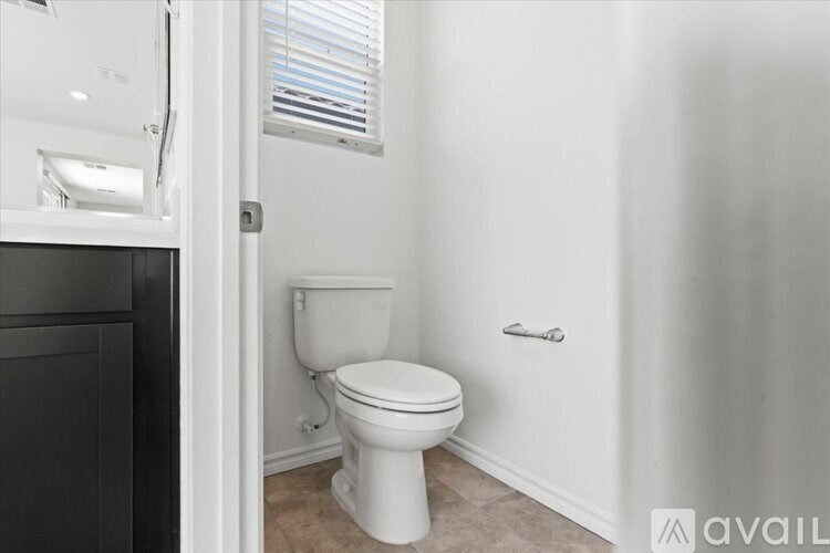 A white toilet in a bathroom with a white wall and a window.