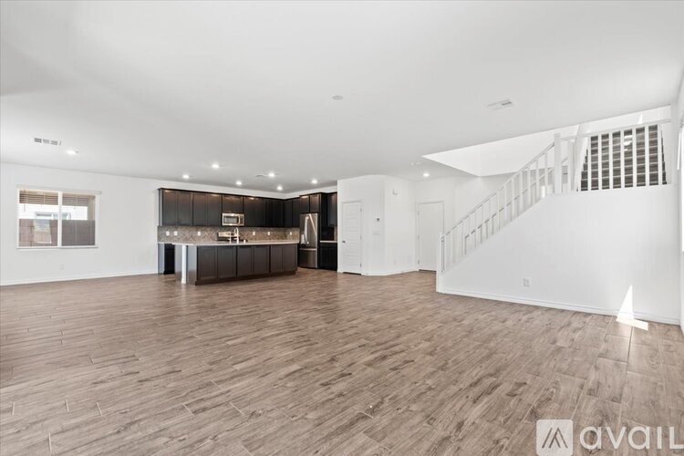 A spacious room with wooden flooring and a staircase on the right side.