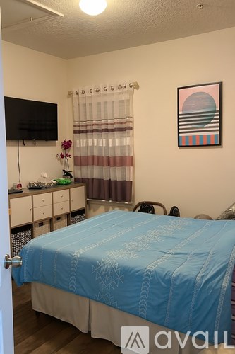 A bedroom with a blue bedspread and a television on the wall.
