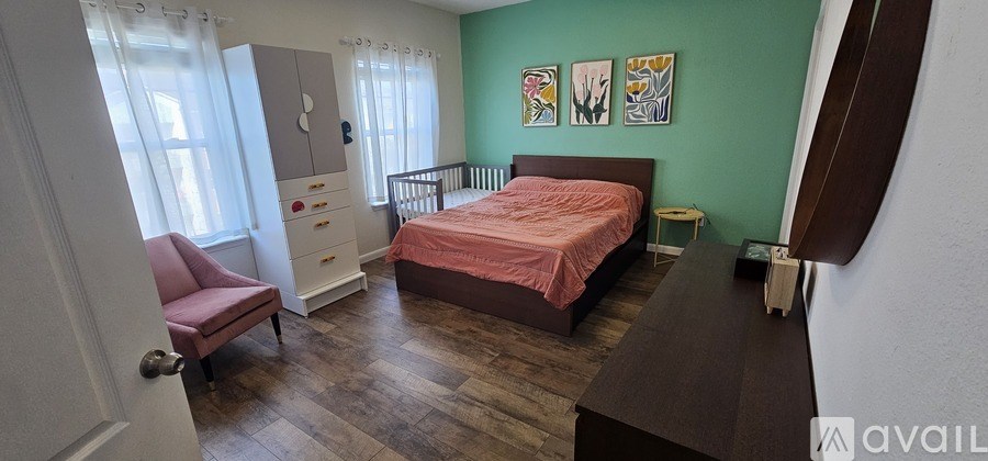 A bedroom with a pink chair, a brown bed, and a white dresser.