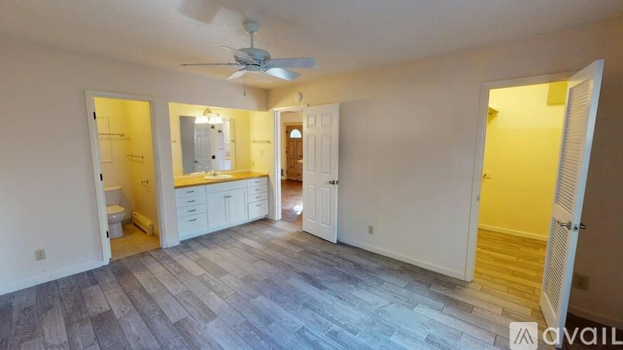 A spacious room with a ceiling fan and lighting, featuring a kitchenette with a sink and cabinets, and a bathroom with a toilet and mirror.