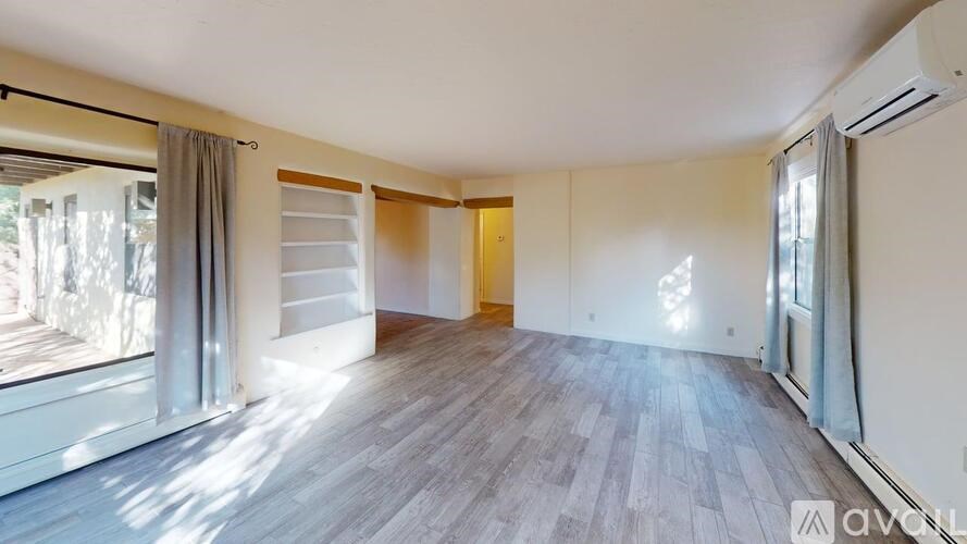 A spacious room with wooden flooring and a large window on the left side.