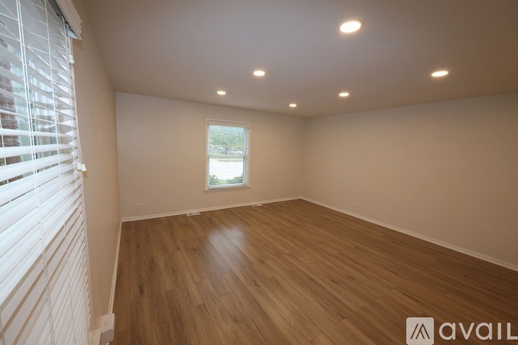 A room with wooden flooring and a window with blinds.