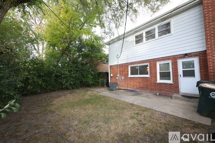 A backyard with a white house, a green trash can, and a tree.