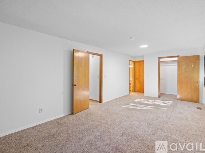 A room with carpeted floor and white walls with four doors.