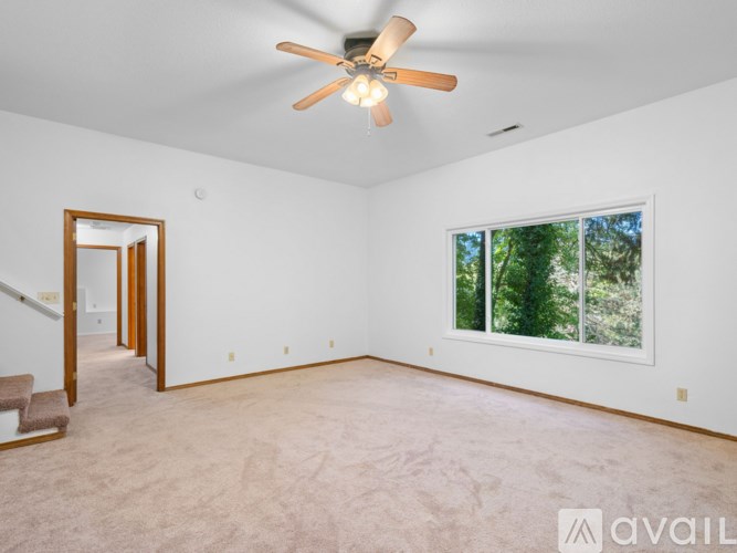 A room with a ceiling fan and a window overlooking trees.