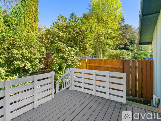 A deck with a white railing and a wooden gate is surrounded by greenery.