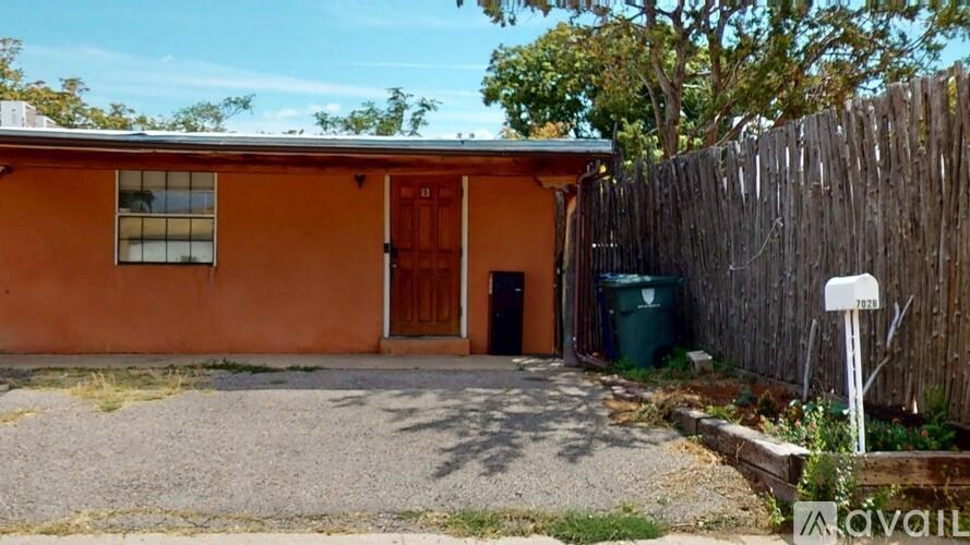 A brown house with a green trash can and a wooden fence.