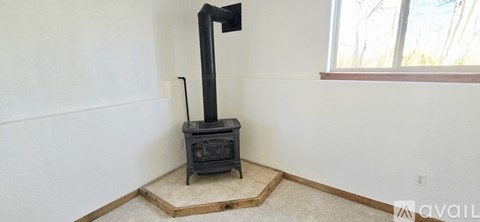 A wood stove is in a corner of a room with a window.