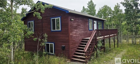 A wooden cabin with a blue trim and a balcony is surrounded by trees.