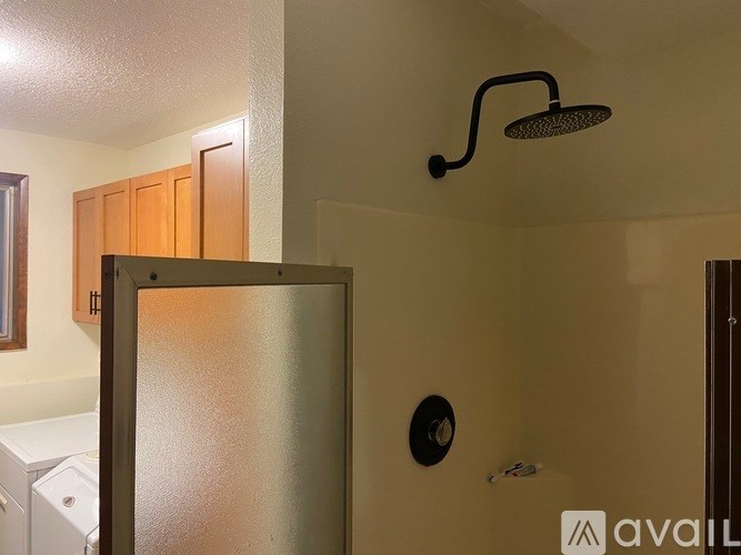 A shower head is mounted on the wall above a silver fridge.