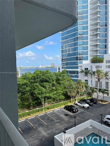 A view from a balcony overlooking a parking lot with a tall building in the background.