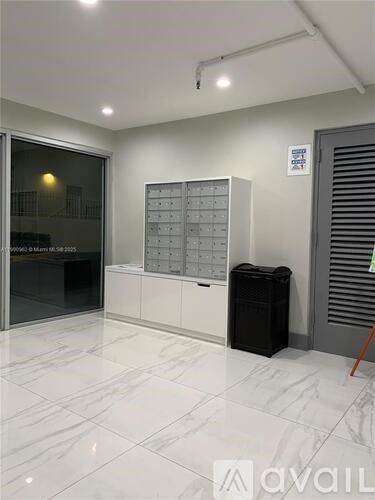 A white room with a black trash bin and a calendar on the wall.