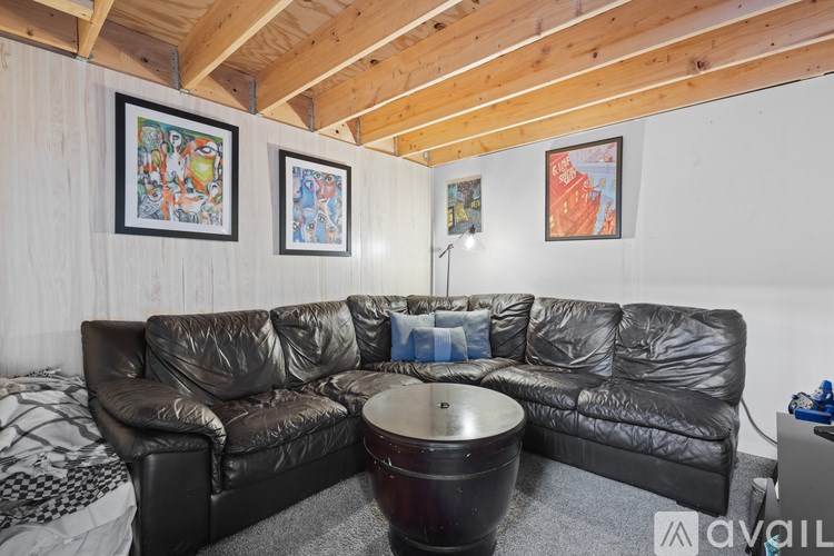 A black leather sectional sofa with a round ottoman in the middle of the room.