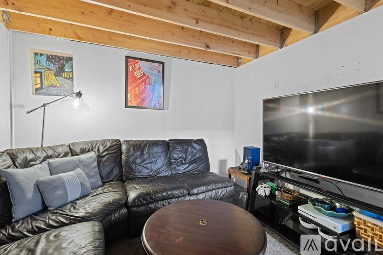 A black leather couch with grey pillows and a wooden coffee table in a room with a wooden ceiling and a painting on the wall.