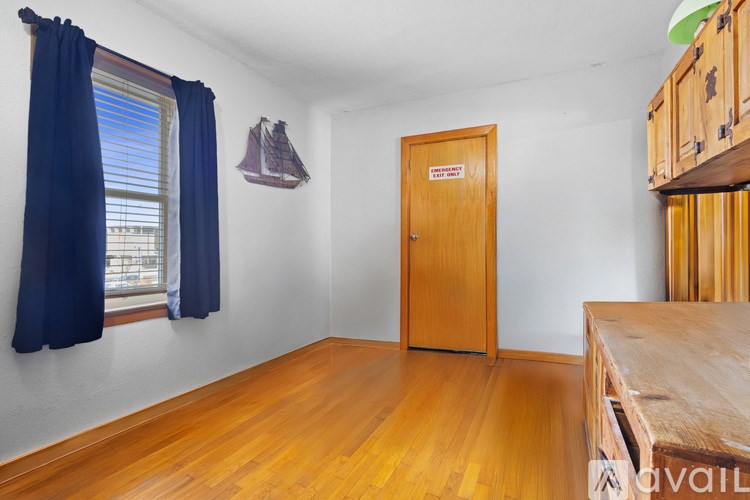 A room with a wooden floor, a window with blue curtains, a wooden wardrobe, and a wooden bed.
