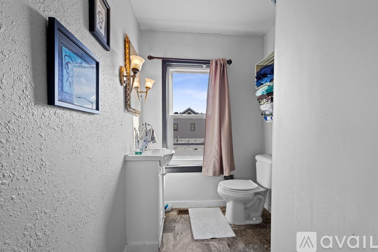 A bathroom with a toilet, sink, and a window with a curtain.