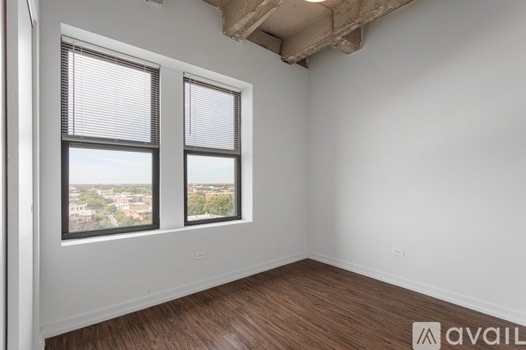 A room with wooden floors and two windows overlooking a cityscape.