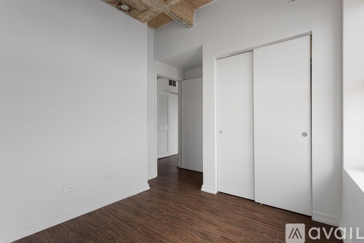 A room with white walls and wooden flooring, featuring a white door and a white wardrobe.