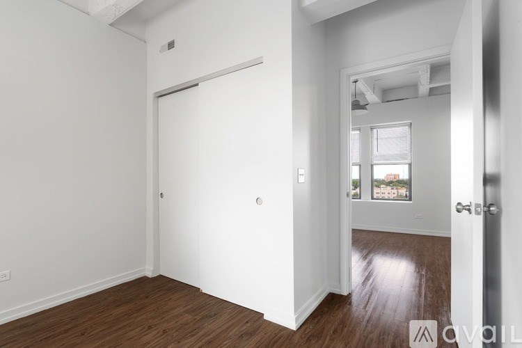 A room with white walls and wooden flooring, with a door on the left and a window on the right.