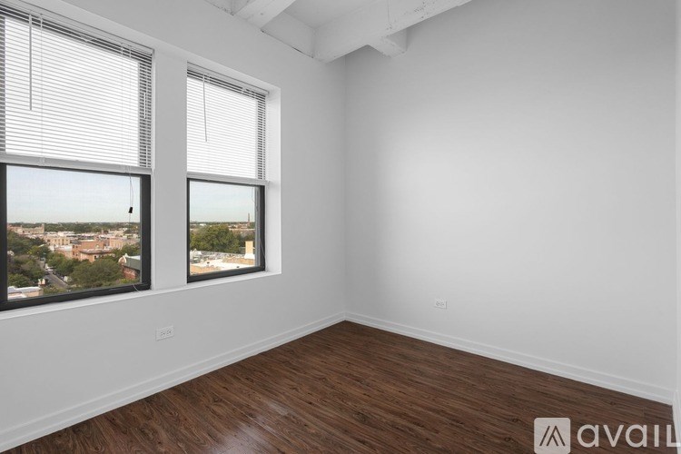 A room with wooden floors and two windows overlooking a cityscape.