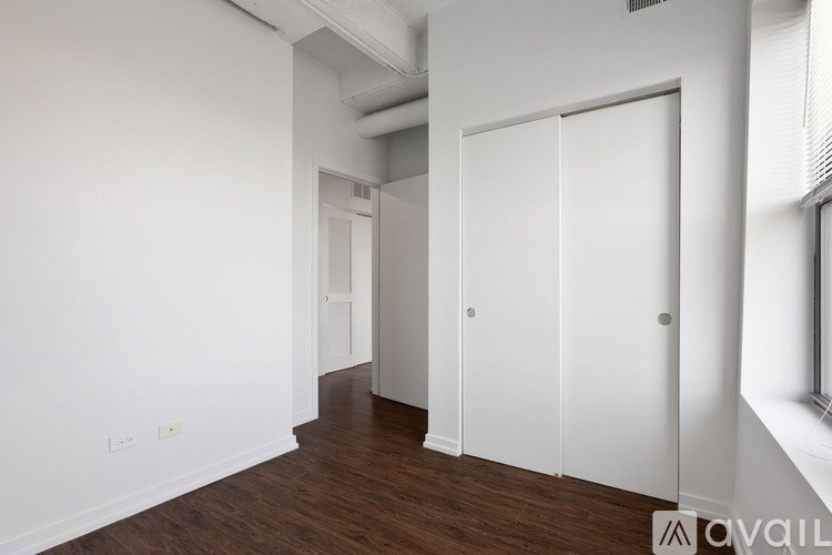 A room with white walls and wooden flooring, featuring a white door and a white cabinet.