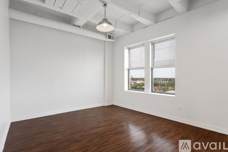 A room with wooden floors and white walls, with a window showing a view of buildings outside.