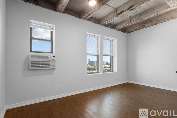 A room with wooden floors and two windows, one of which has blinds.