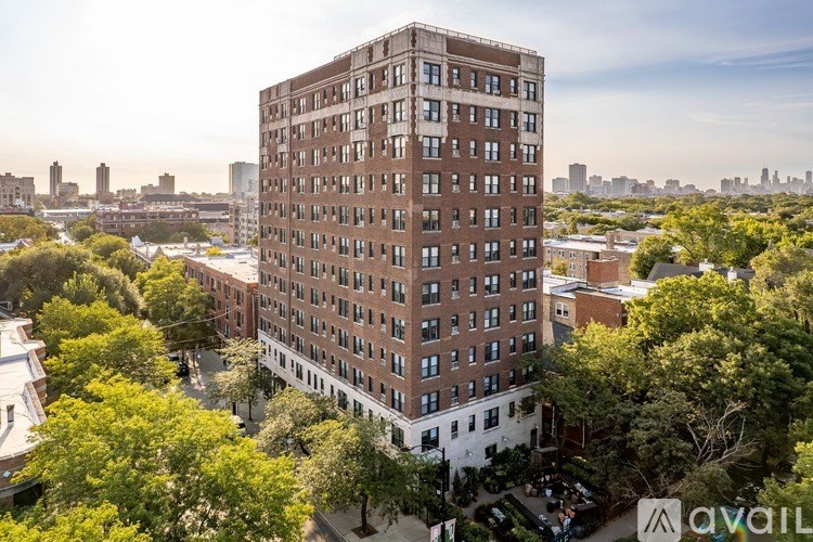 A tall brown building with many windows is surrounded by trees.